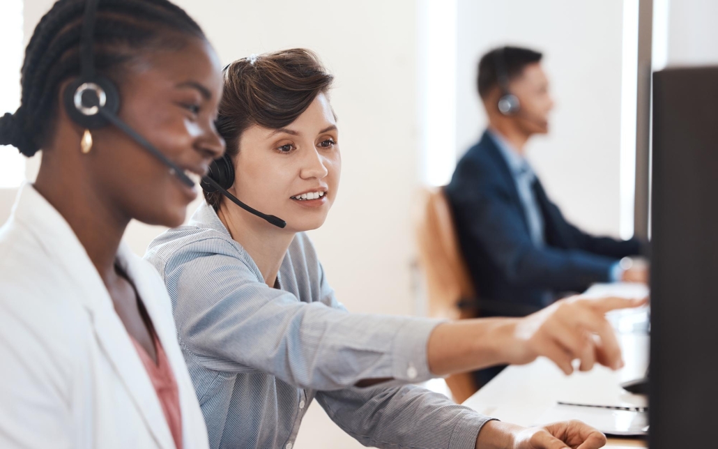 Workers With Headsets Looking At Computer While On Calls