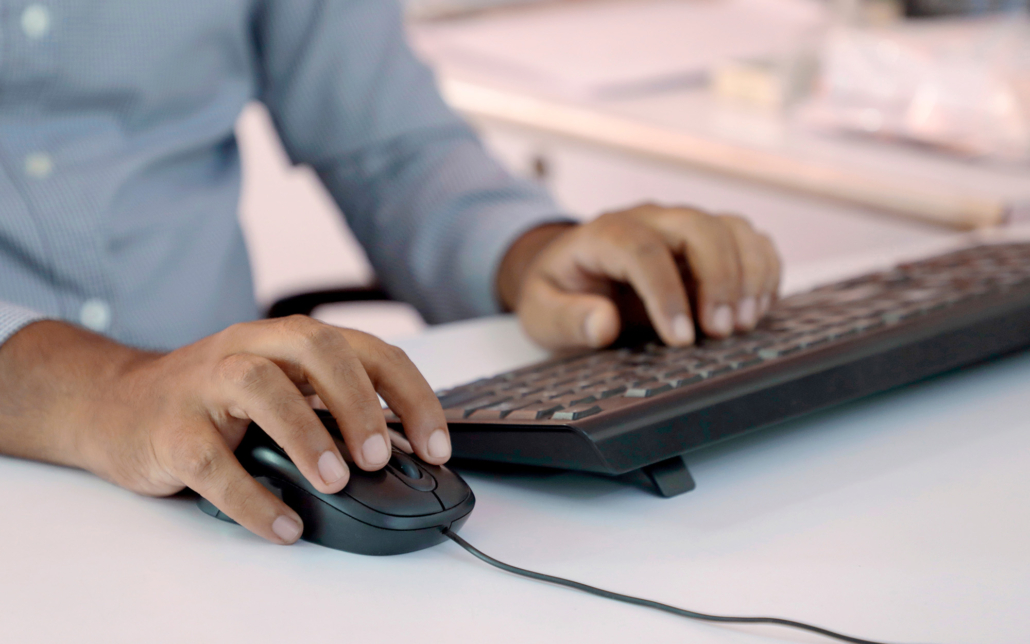 Businessman Typing On Keyboard And Scrolling Mouse At Desk In Office