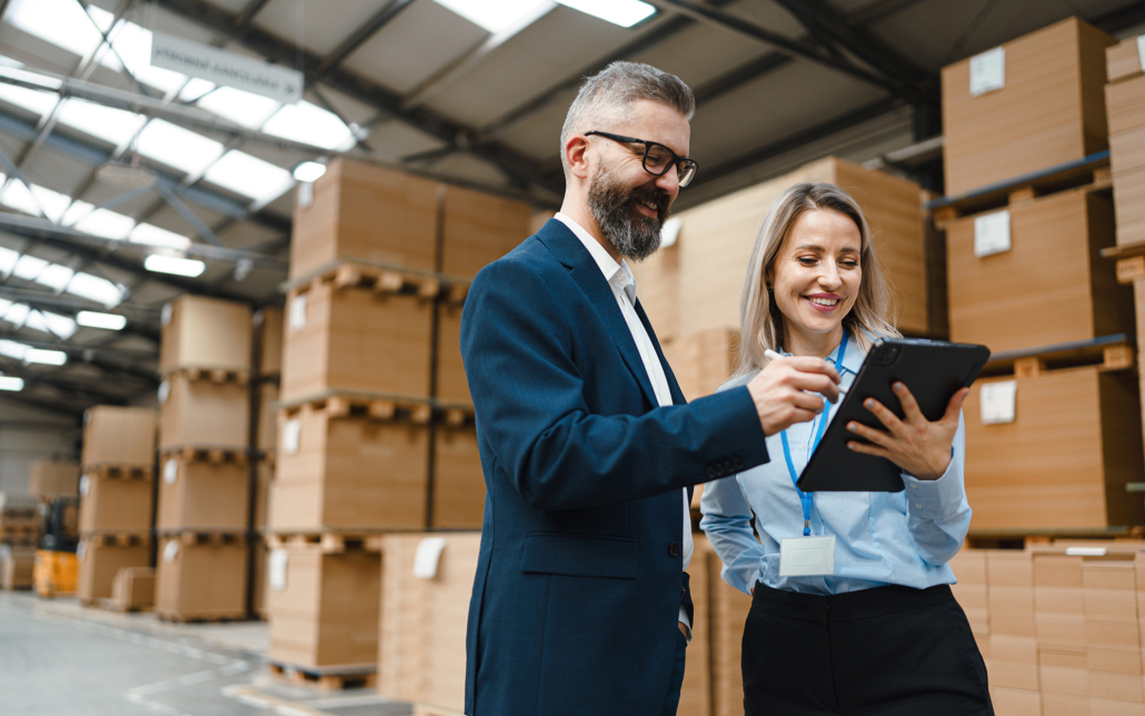 Two People In Warehouse Look At Tablet