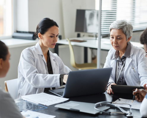 Brunette Female Clinician In Lab Coat Pointing At Laptop Screen